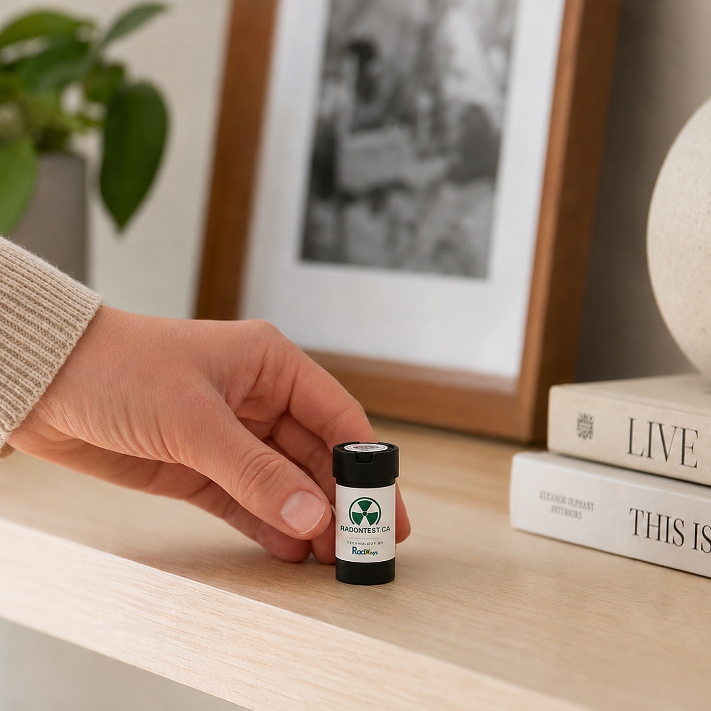 Hand placing the RadonTest.ca alpha-track radon detector on a wood shelf in a home, showing its compact, unobtrusive size